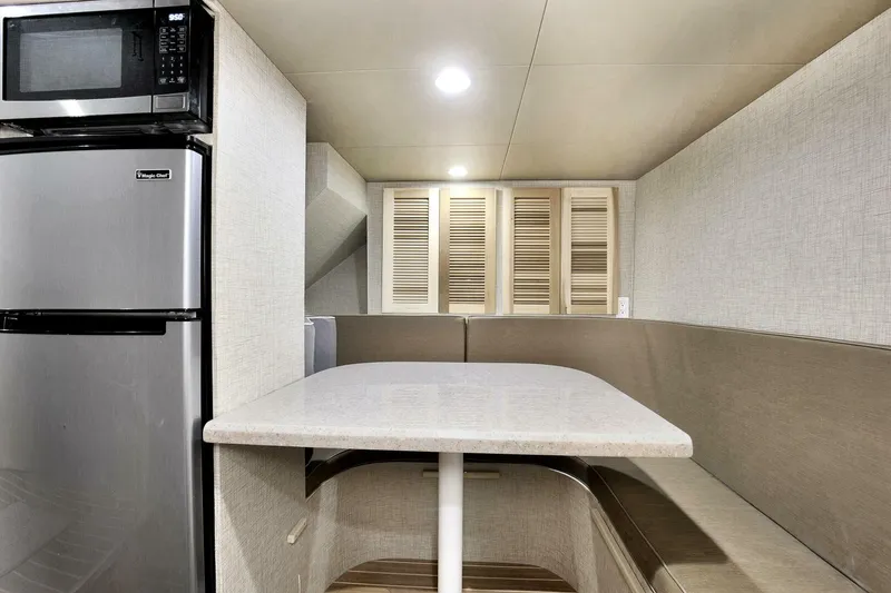 Slide: The Image of 1983 Broward 108 Cockpit Motor Yacht interior dining area with table, bench seating, and kitchen appliances. - 30