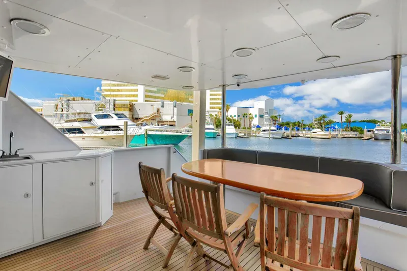 Slide: The Image of Spacious deck of 1983 Broward 108 Cockpit Motor Yacht with wooden chairs and marina view. - 35