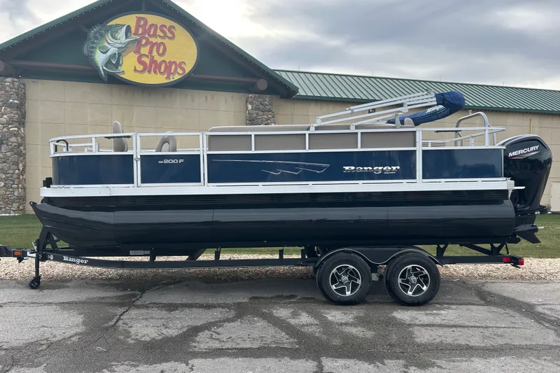 The Image of 2024 Ranger Reata 200F pontoon boat on trailer outside Bass Pro Shops. - 0