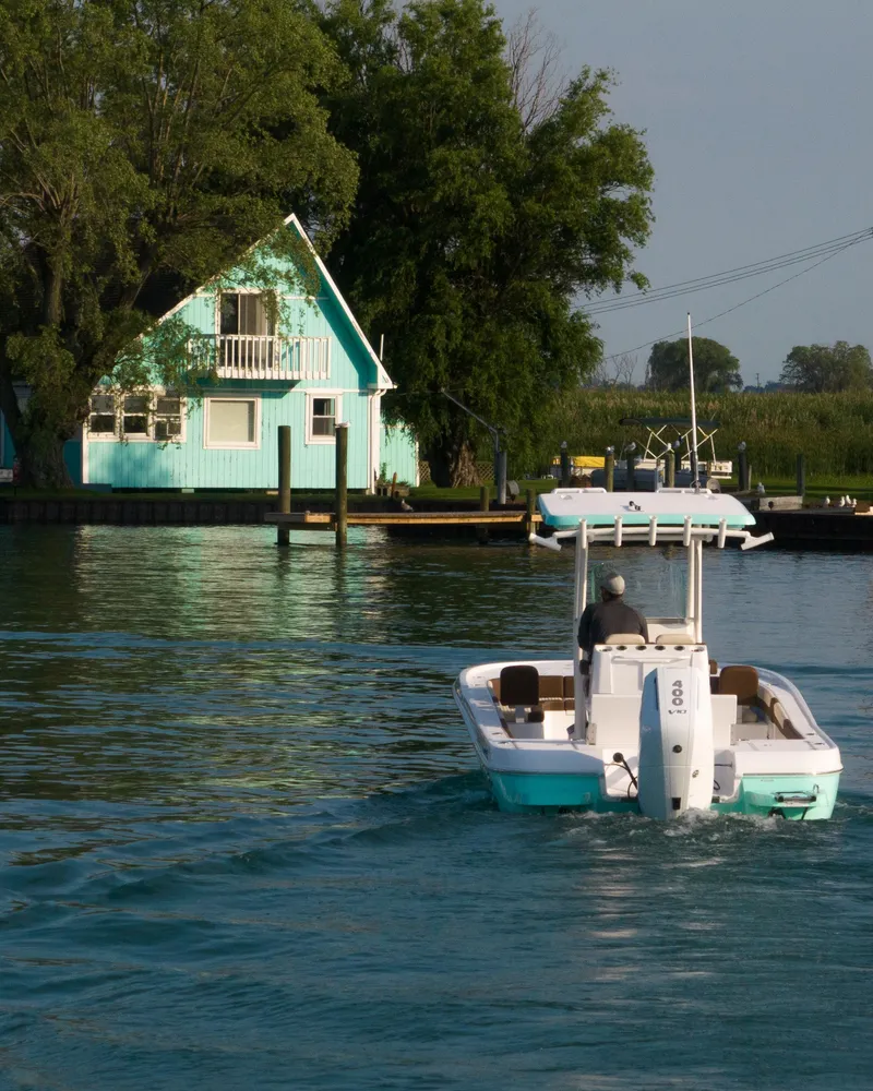 Slide: The Image of 2024 Caymas 28 Hybrid boat cruising near a turquoise lakeside house. - 11