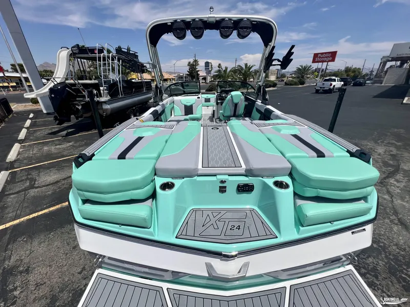 Slide: The Image of 2023 MasterCraft XT24 boat with teal and gray seating, parked outdoors. - 2