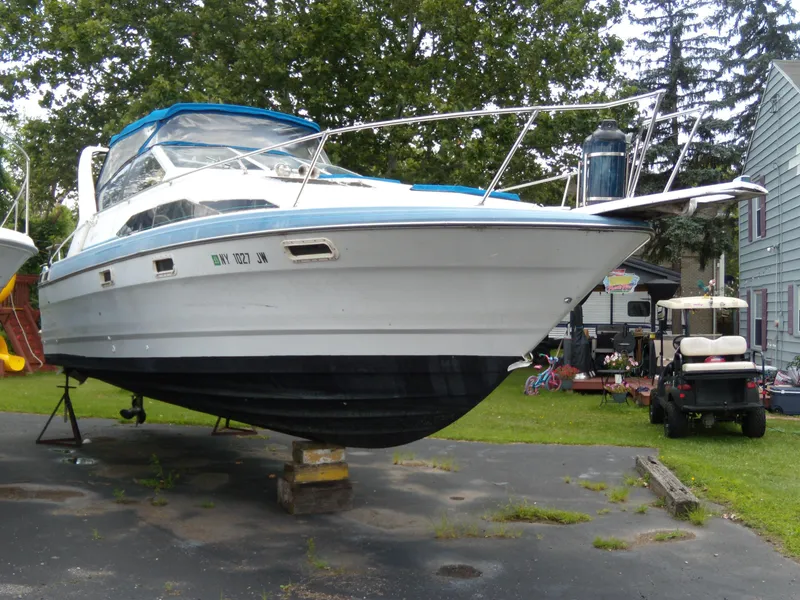 The Image of 1988 Bayliner 2655 Ciera Sunbridge boat on land, blue canopy, parked near trees. - 1
