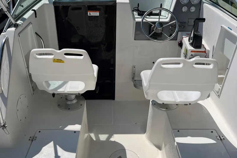 Slide: The Image of 2005 Aquasport 215 Explorer boat cockpit with dual white captain chairs and steering console. - 8