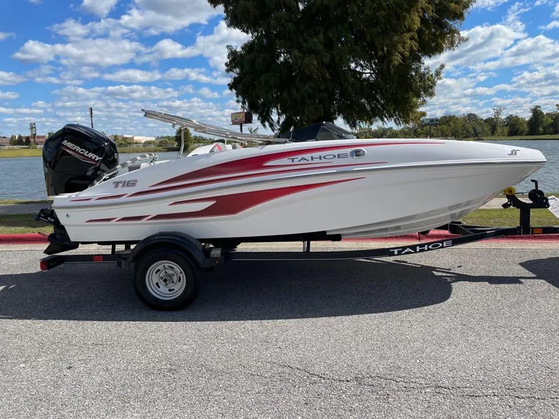 The Image of 2024 Tahoe T16 boat with red and white design on a trailer by a lake. - 0