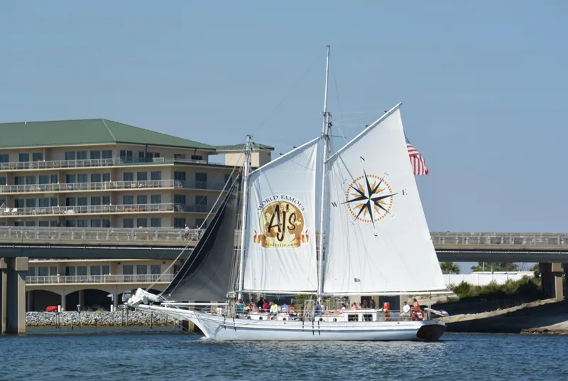 The Image of Custom 1996 Biloxi Schooner sailing near a waterfront building on a sunny day. - 1