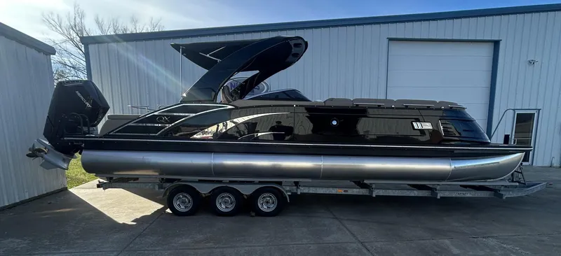 Slide: The Image of 2023 Bennington 28 QXSBW pontoon boat on a trailer, parked outside a warehouse. - 0