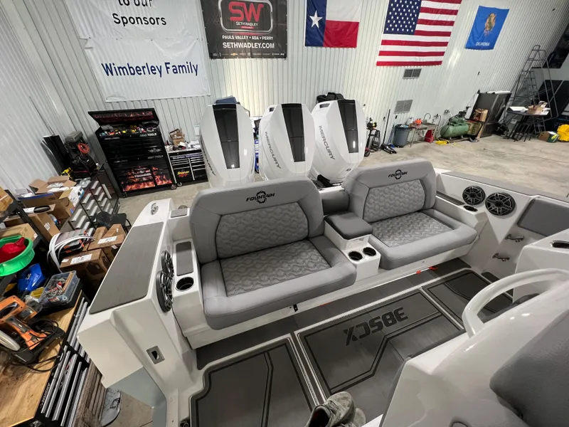 Slide: The Image of 2023 Fountain 38 SCX boat interior with seating, engines, and flags in a workshop. - 25