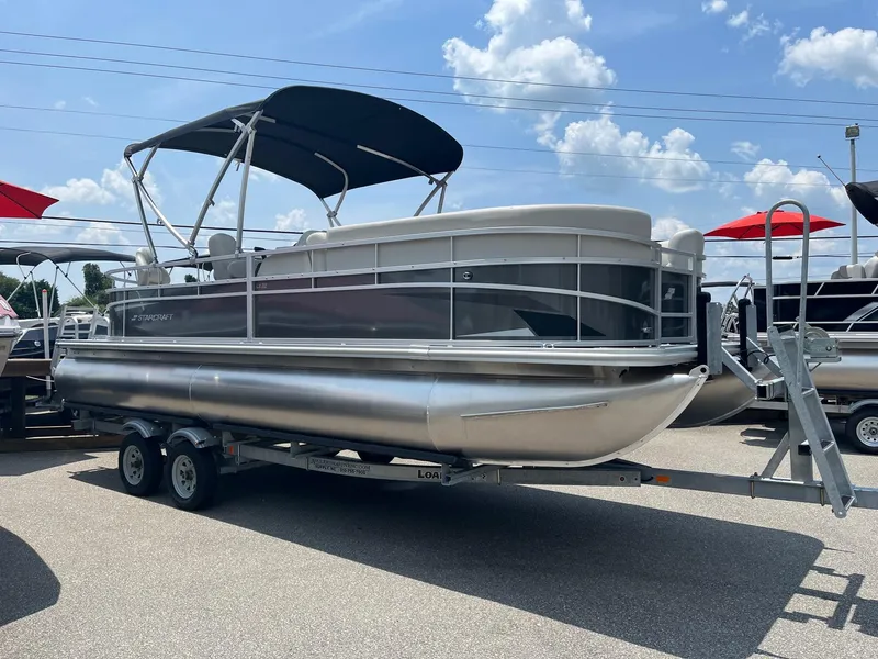 Slide: The Image of 2024 Starcraft LX22 F pontoon boat on a trailer under a sunny sky. - 1