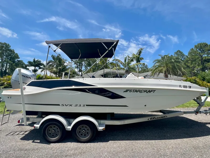 Slide: The Image of 2021 Starcraft 211 SVX boat on a trailer with a canopy, parked outdoors. - 5