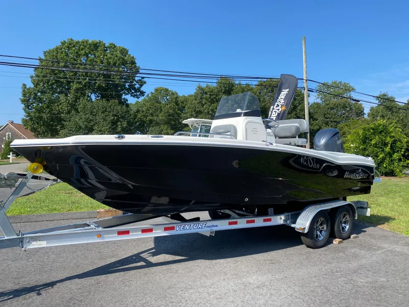 The Image of 2024 NauticStar 211 Hybrid boat on a trailer, parked outdoors. - 1