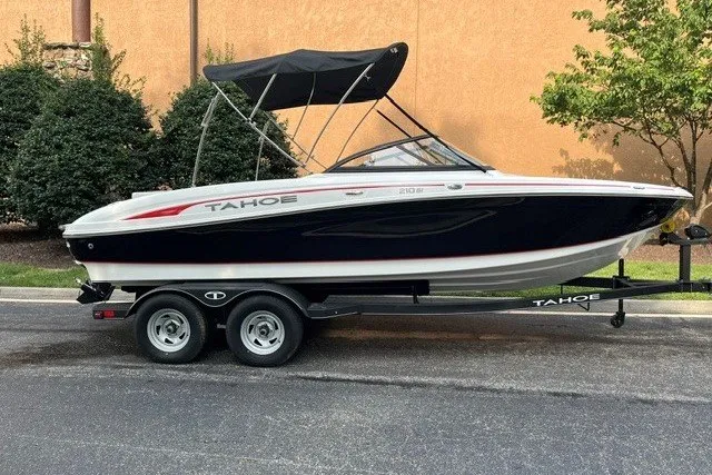 The Image of 2024 Tahoe 210 Si boat on trailer, black and white design, parked outdoors. - 0