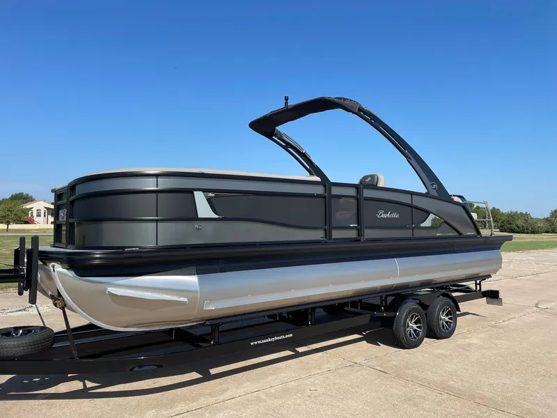 Slide: The Image of 2024 Barletta Lusso 25UCA pontoon boat on a trailer under a clear blue sky. - 2
