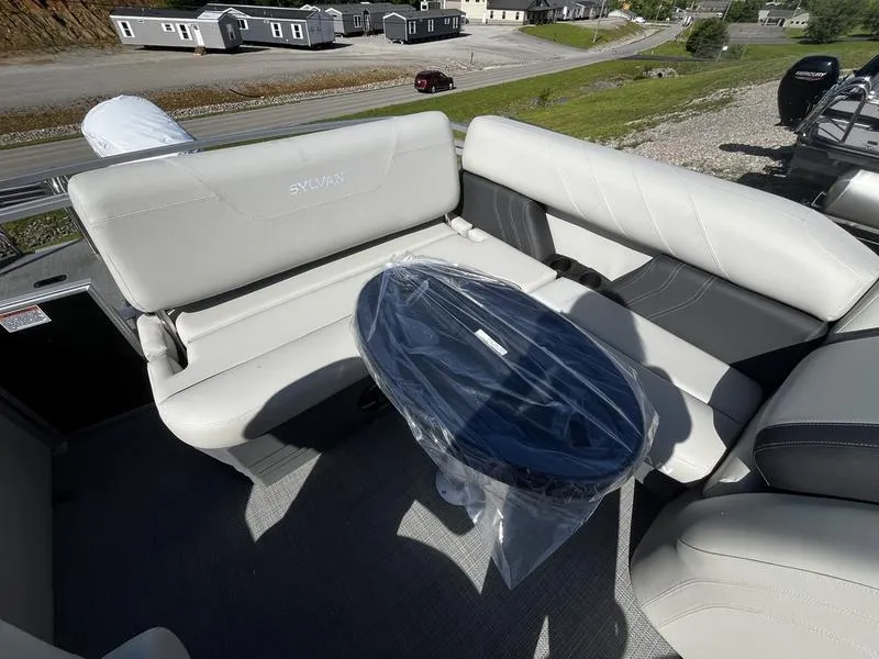 Slide: The Image of 2024 Sylvan Mirage 8522 CLZ boat interior with cushioned seating and a covered table. - 3