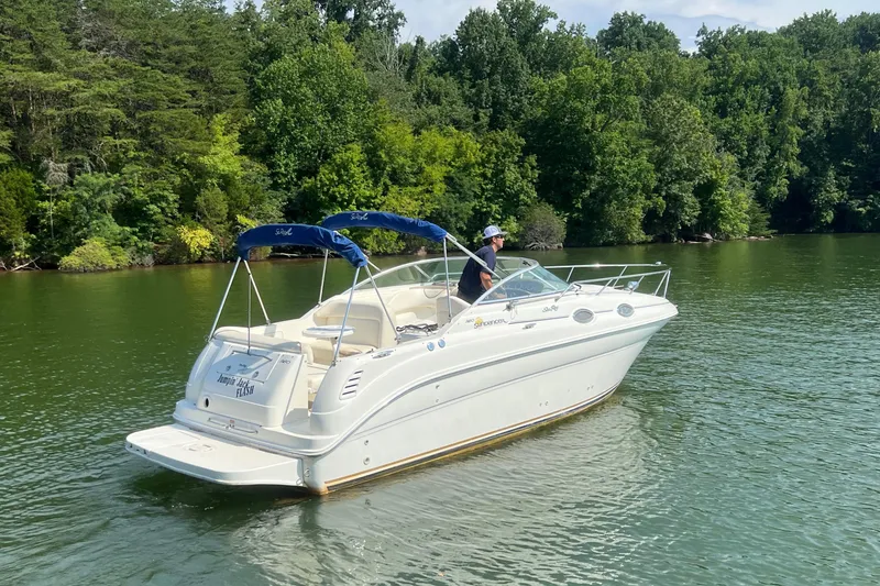 Slide: The Image of 2001 Sea Ray 260 Sundancer boat cruising on a lake with lush green trees in the background. - 2