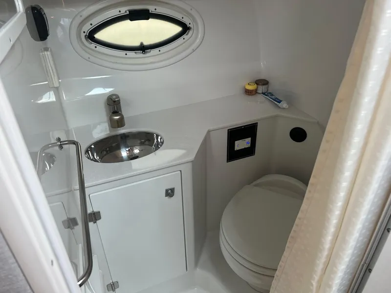 Slide: The Image of 2019 Monterey 295 Sport Yacht bathroom with sink, toilet, and porthole window. - 28