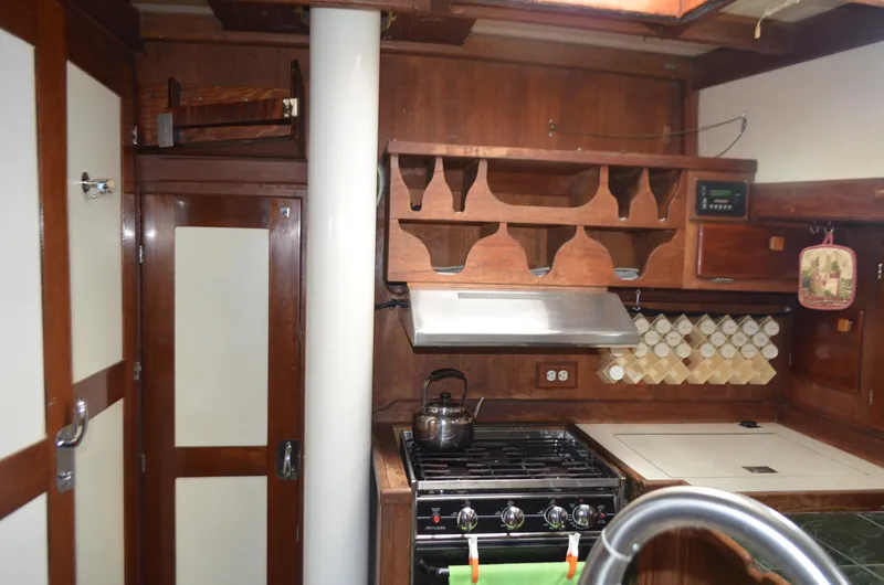 Slide: The Image of 1973 Skookum Ketch kitchen with wooden cabinets, stove, and spice rack. - 15