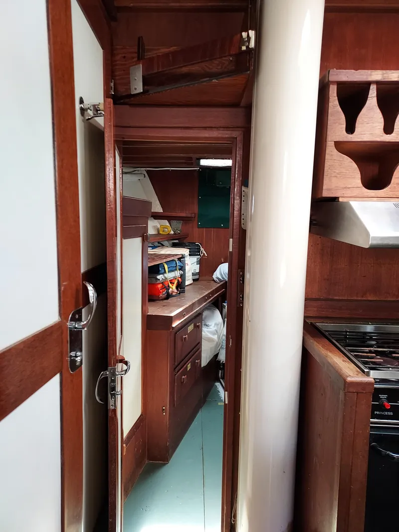 Slide: The Image of Interior of a 1973 Skookum Ketch sailboat, featuring wooden cabinetry and compact kitchen space. - 24