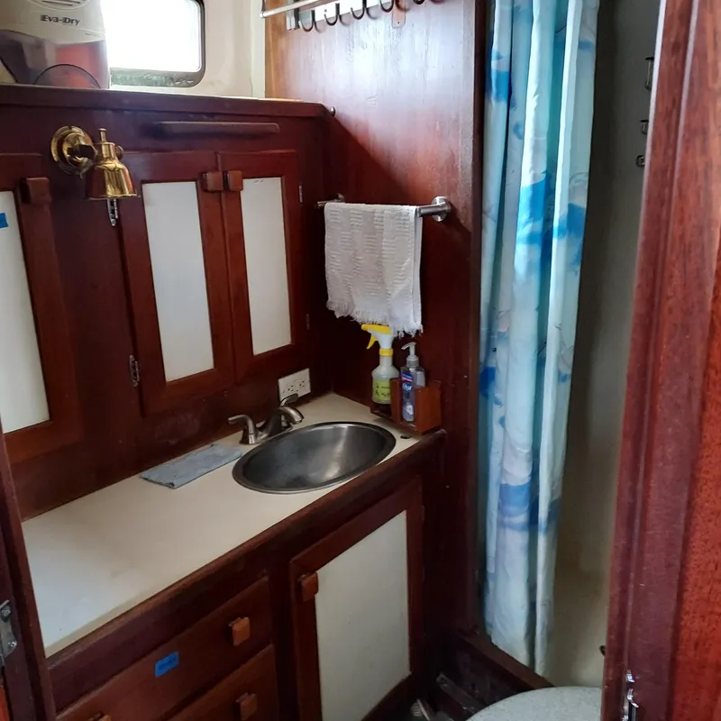 Slide: The Image of 1973 Skookum Ketch bathroom with wooden cabinets, sink, and shower curtain. - 43