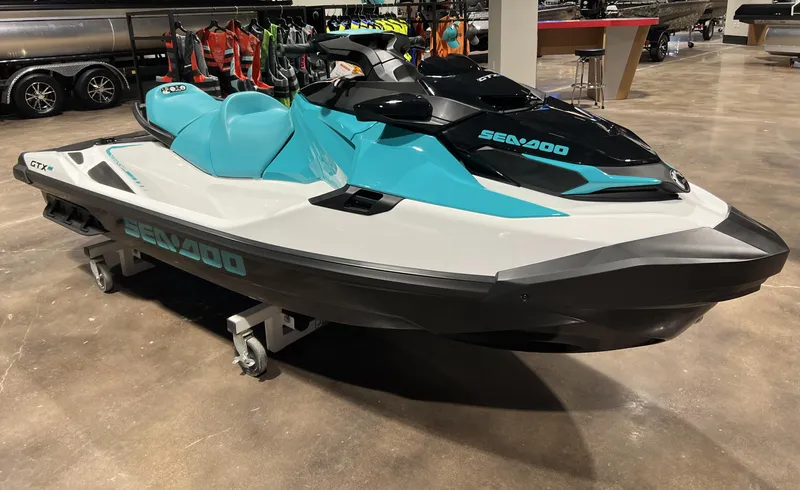 Slide: The Image of 2022 Sea-Doo GTX PRO 130 jet ski in showroom, teal and black design. - 1