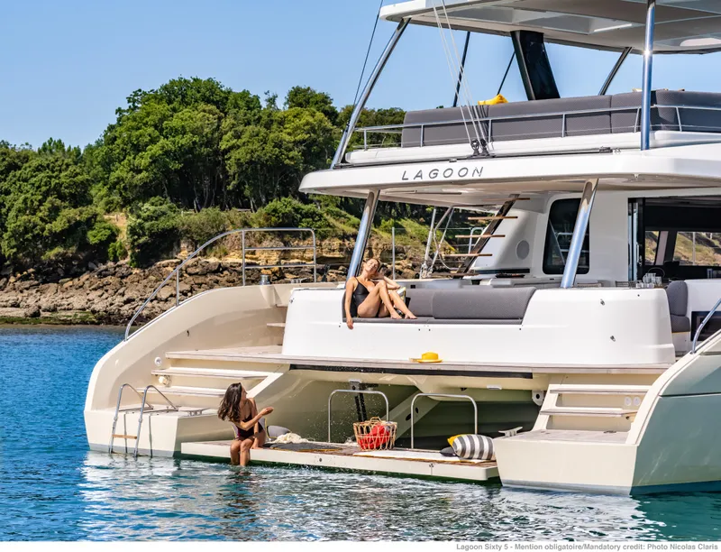 Slide: The Image of 2025 Lagoon Sixty5 yacht with people relaxing on deck, anchored near lush shoreline. - 4