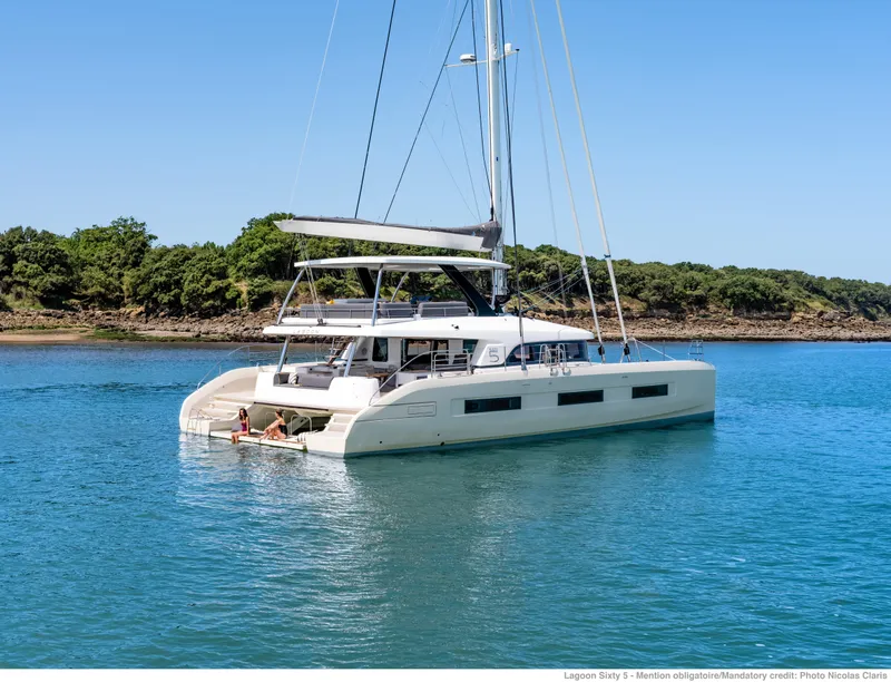 Slide: The Image of 2025 Lagoon Sixty5 catamaran sailing on calm blue waters near a lush green shoreline. - 5
