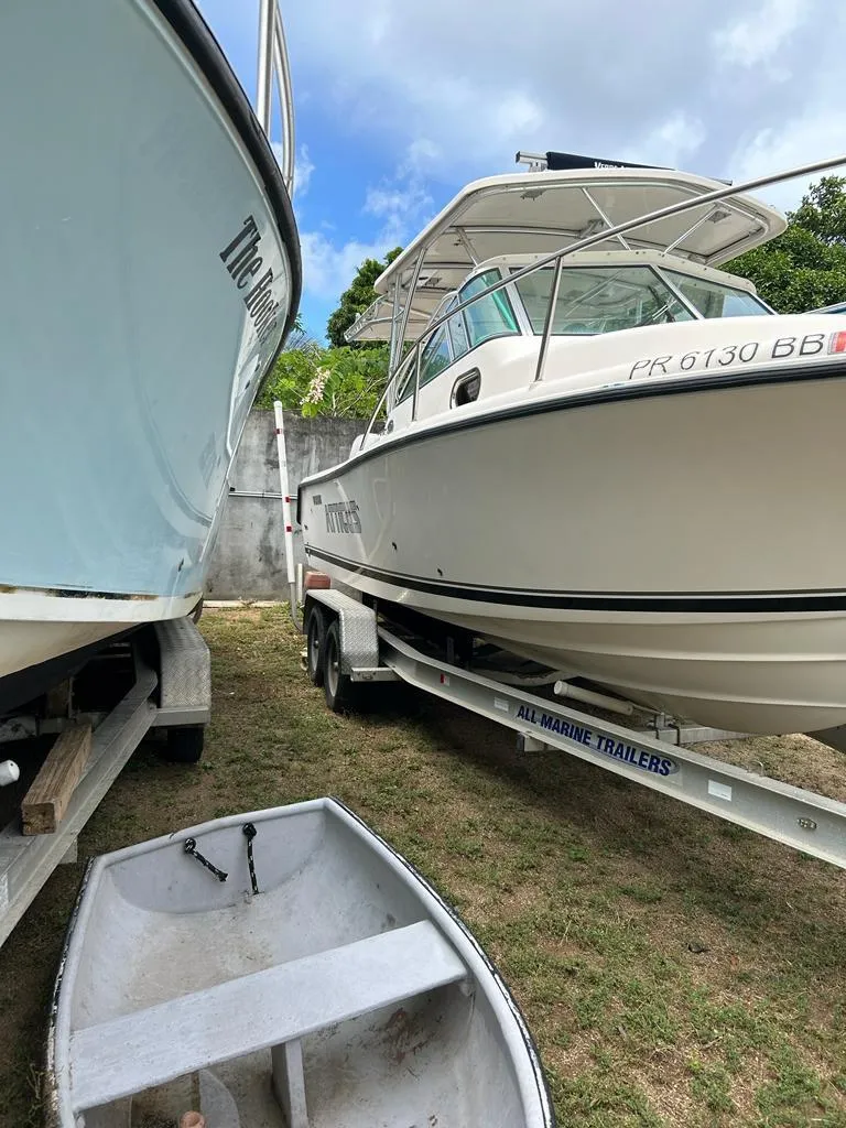 Slide: The Image of 2012 Pursuit 255 boat on trailer, parked beside another boat, with a small dinghy in foreground. - 5