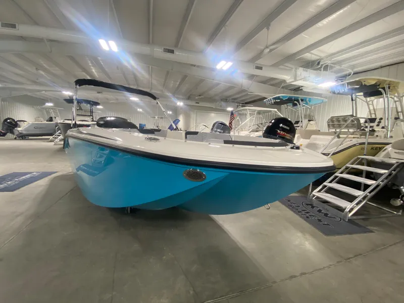 Slide: The Image of 2024 Bayliner Element M19 boat in showroom, blue hull, bimini top, outboard motor. - 2