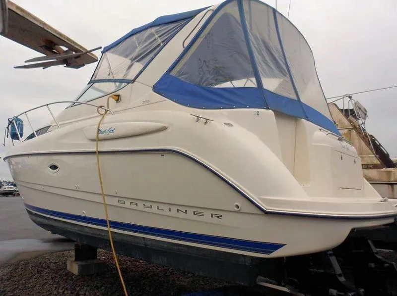Slide: The Image of 2006 Bayliner 305 boat with blue canopy, docked on land. - 24