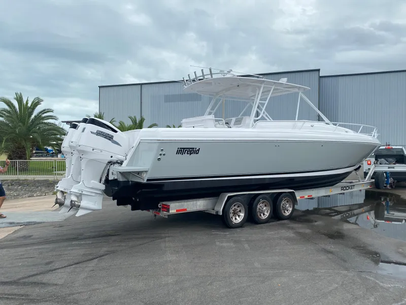 Slide: The Image of 2001 Intrepid 377 Walkaround boat on a trailer, parked outdoors near a warehouse. - 17