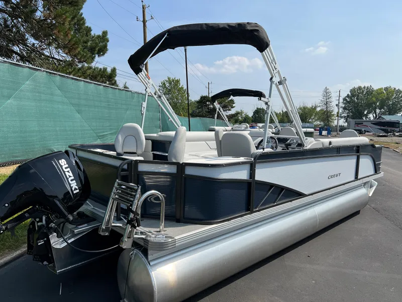 Slide: The Image of 2024 Crest Classic Fish 220 pontoon boat with Suzuki outboard motor, parked outdoors. - 2