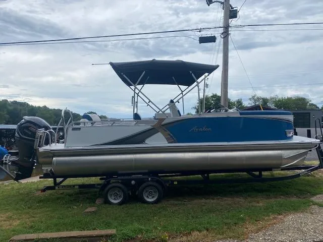 Slide: The Image of 2024 Avalon LSZ 2385 VRL pontoon boat on trailer, blue and silver design, parked outdoors. - 4