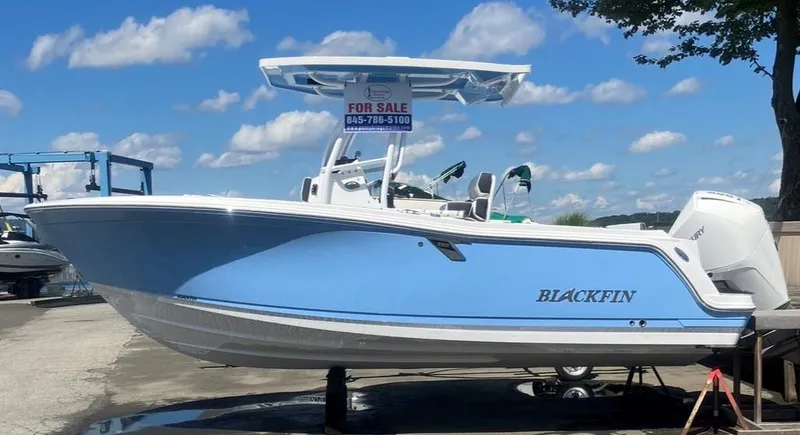 The Image of 2024 Blackfin 222 CC boat for sale, blue hull, parked on a trailer, clear sky background. - 0