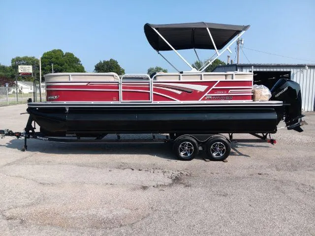 Slide: The Image of 2023 Ranger Reata 223C pontoon boat with red accents and black trailer, parked outdoors. - 3