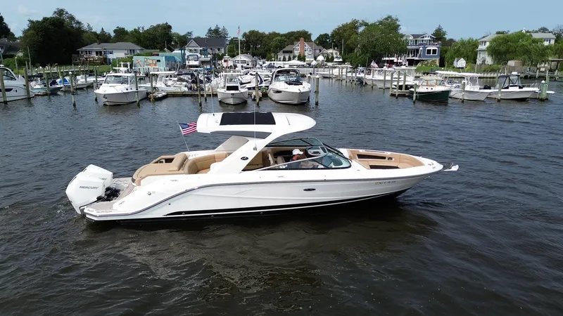 The Image of 2023 Sea Ray SLX 310 boat cruising in a marina with multiple docked boats. - 0