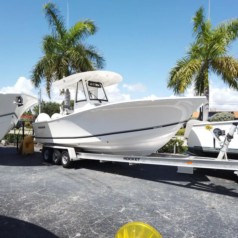 The Image of 2026 Regulator 28 boat on trailer, parked under palm trees, clear blue sky. - 0