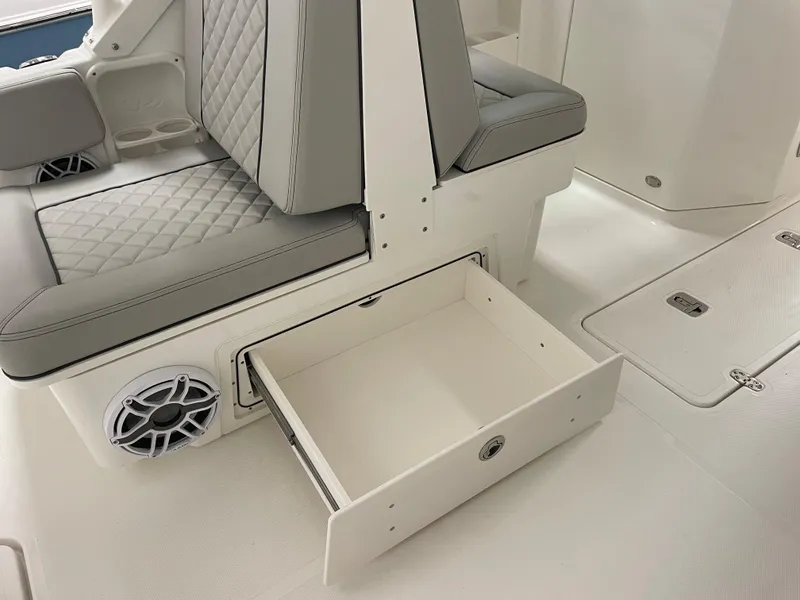Slide: The Image of 2024 Pursuit DC 246 Dual Console boat interior with open storage drawer and cushioned seating. - 23