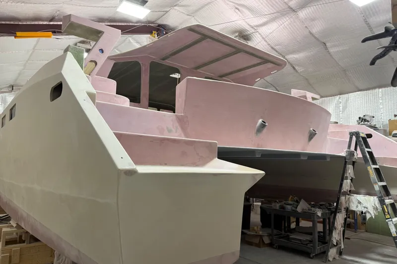 Slide: The Image of 2026 Schionning Arrow 1280 S catamaran under construction in a workshop. - 100