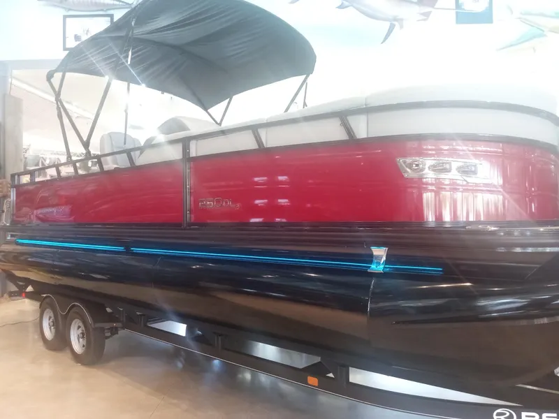 Slide: The Image of 2024 Regency 250 DL3 pontoon boat with red and black exterior on a trailer. - 3
