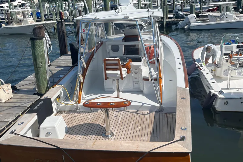 Slide: The Image of 1985 Rybovich Walkaround boat docked at a marina, featuring a spacious deck and fishing chair. - 22