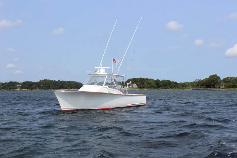 Slide: The Image of 1985 Rybovich Walkaround boat on calm waters with a scenic shoreline background. - 3
