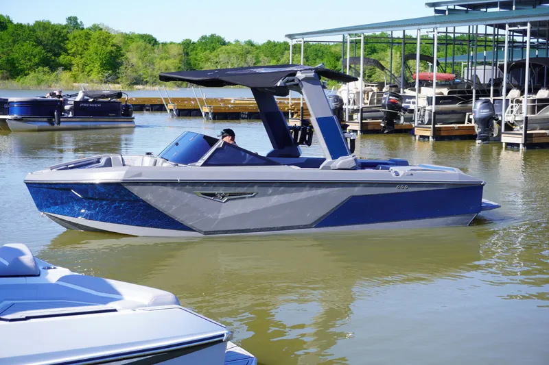 Slide: The Image of 2024 Nautique S23 boat on a calm lake near a marina. - 0
