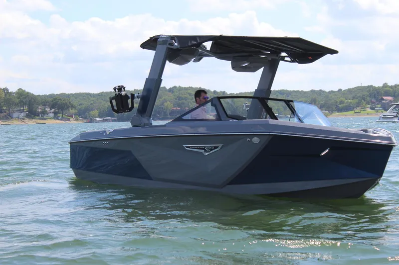 Slide: The Image of 2024 Nautique S23 boat cruising on a lake with a person at the helm. - 2