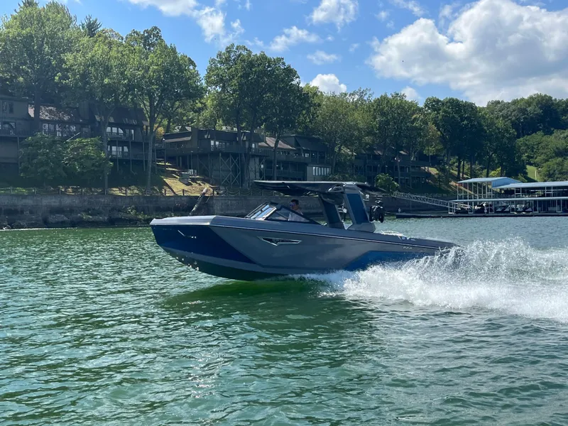 Slide: The Image of 2024 Nautique S23 boat cruising on a lake near waterfront homes. - 5