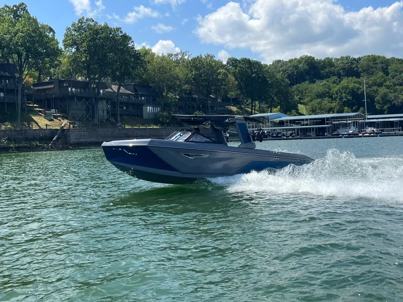 Slide: The Image of 2024 Nautique S23 boat cruising on a lake with scenic shoreline. - 6