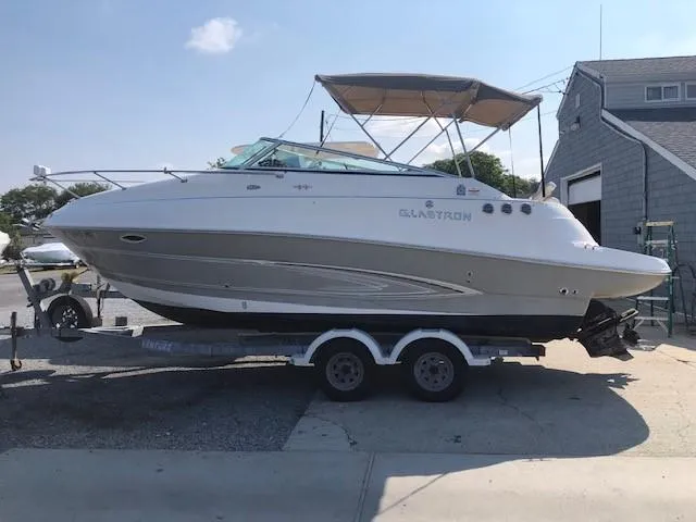 The Image of 2008 Glastron GS 259 boat on a trailer, parked near a building. - 0