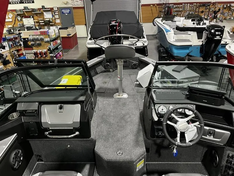 Slide: The Image of 2024 Lund 1875 Pro V Sport boat interior at a showroom, featuring steering console and seating. - 5