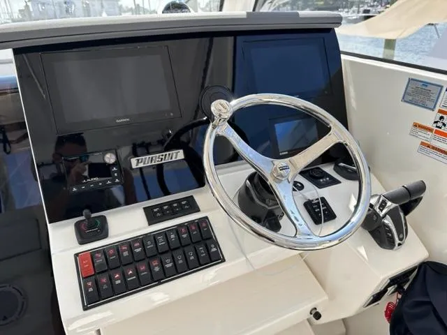 Slide: The Image of 2022 Pursuit OS 355 boat helm with steering wheel, control panel, and navigation screens. - 11