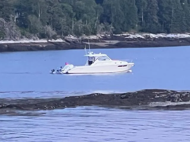 Slide: The Image of 2022 Pursuit OS 355 boat on calm water near a forested shoreline. - 3