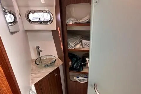 Slide: The Image of 2022 Pursuit OS 355 bathroom with sink, storage shelves, and porthole window. - 48
