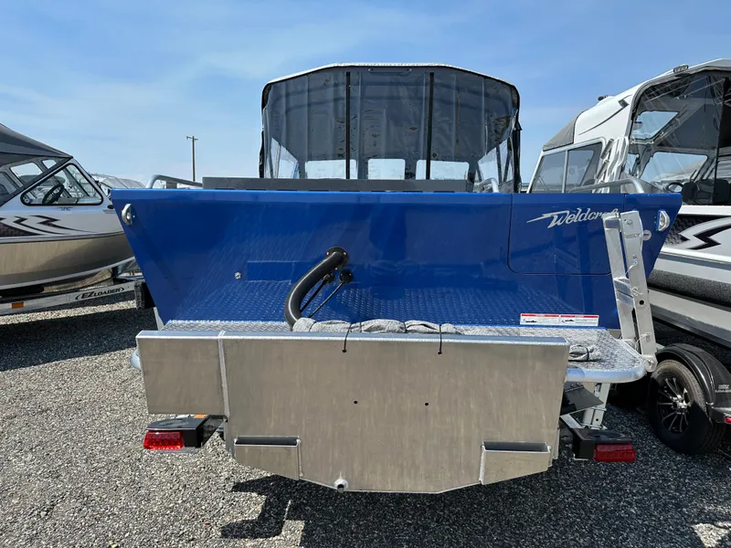Slide: The Image of 2024 Weldcraft 220 Maverick boat, rear view, blue exterior, parked on gravel lot. - 2